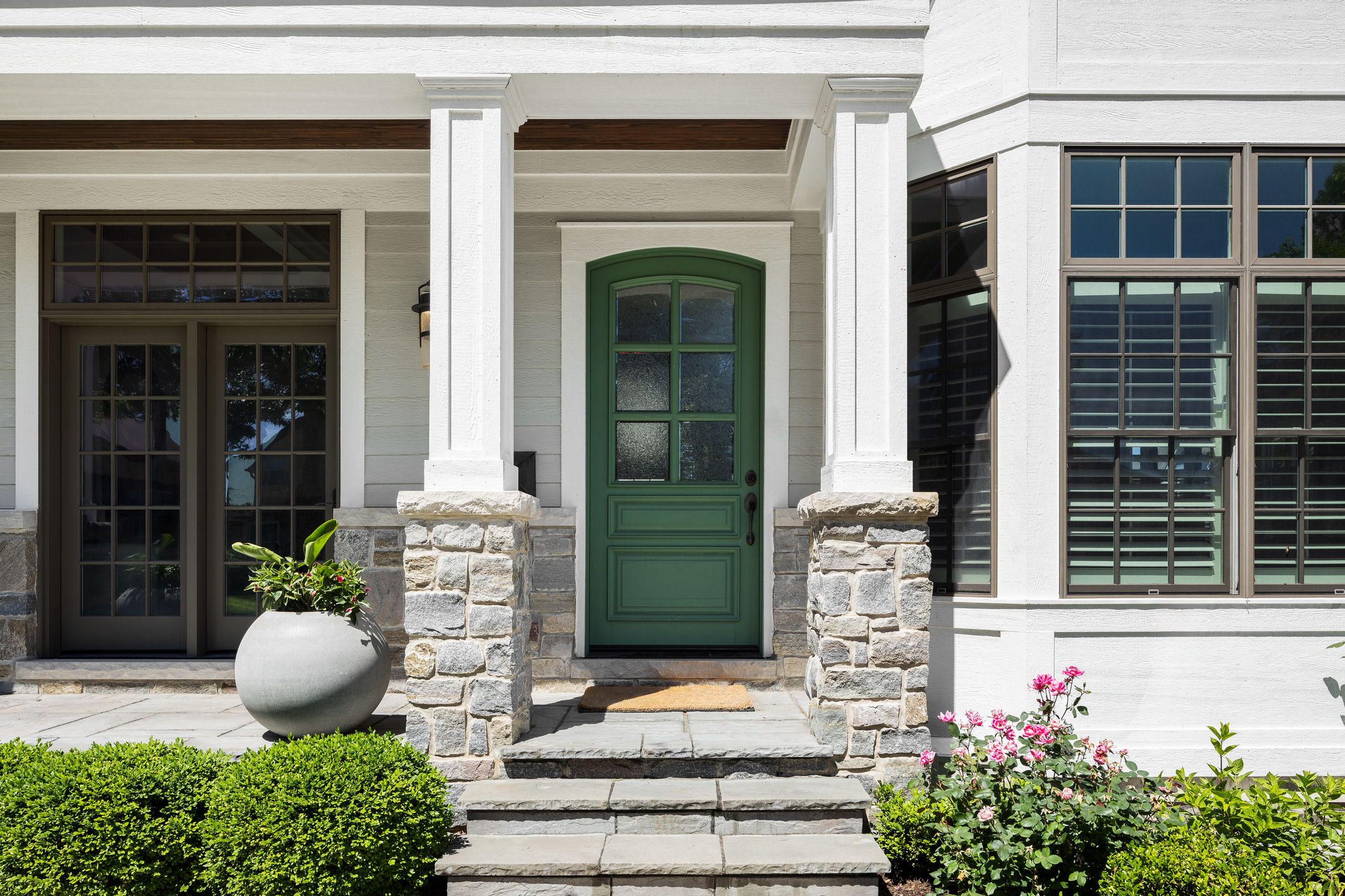 A green front door on a white modern farmhouse with a covered front porch. replace-windows-and-doors